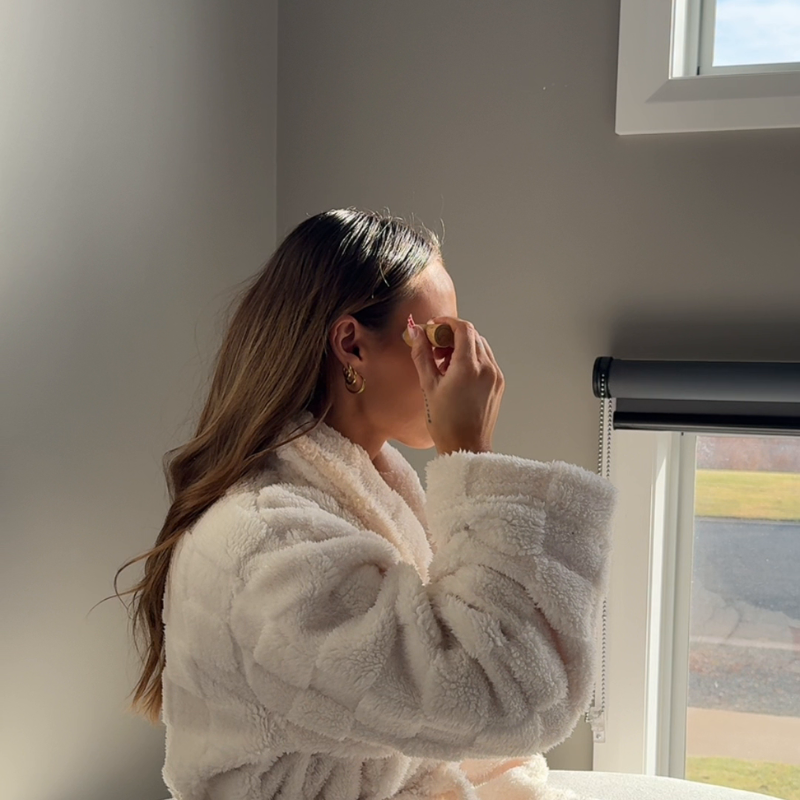 Woman in white rode applying an essential oil roller to temples