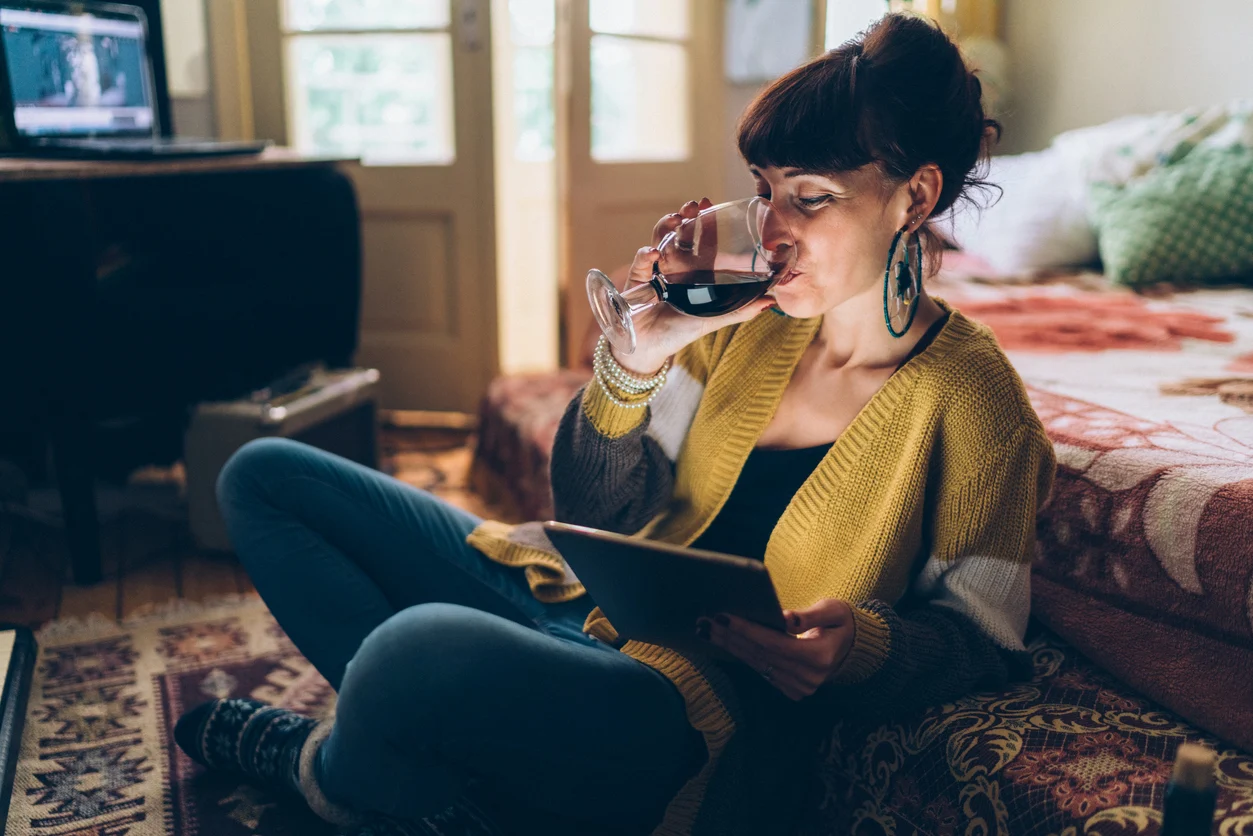 Woman drinking glass of red wine with smart tablet in hand. Source: Sleep Foundation