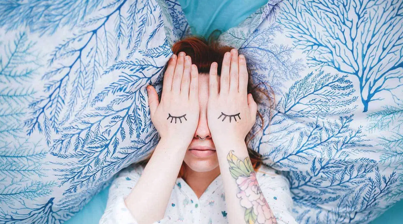 a woman lying on bed covering her eyes with her hands