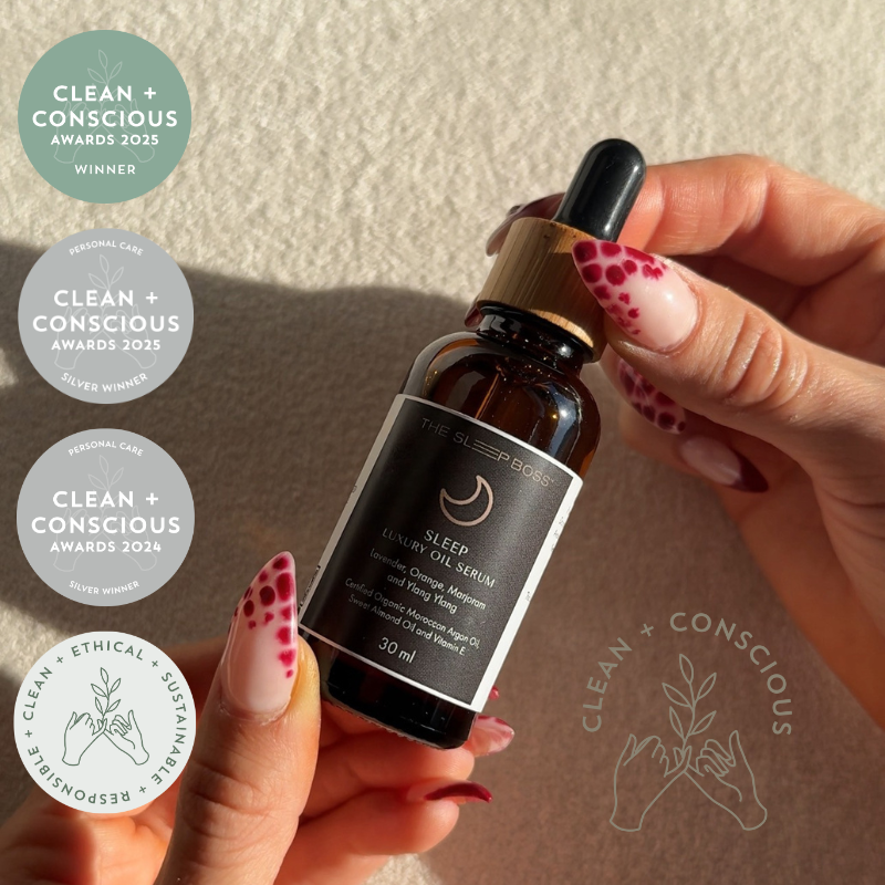 Hand holding a bottle of 'Sleep' Luxury serum with 'Clean + Conscious' awards on a beige background