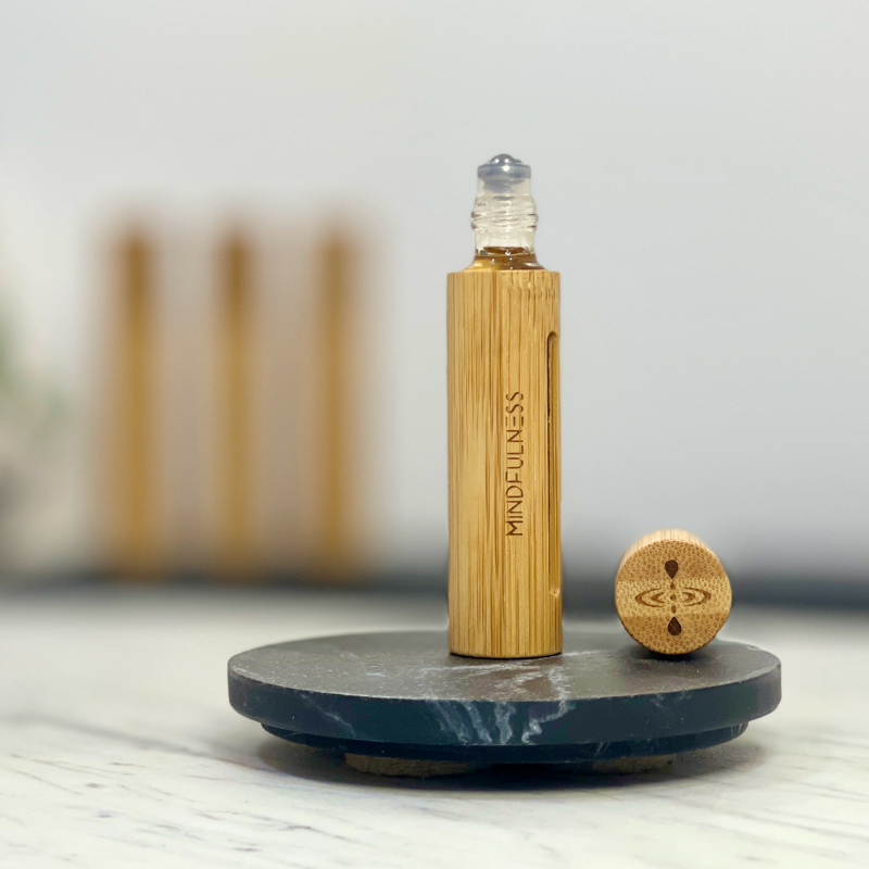 Essential oil roller, Mindfulness Blend, in a sleek bamboo case with a cap opened to show the ball roller.