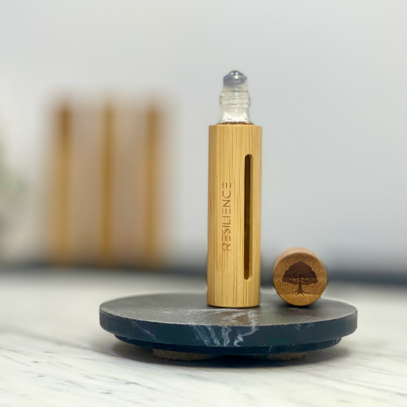 Essential oil roller, Resilience Blend, in a sleek bamboo case with opened cap to show the roller ball.