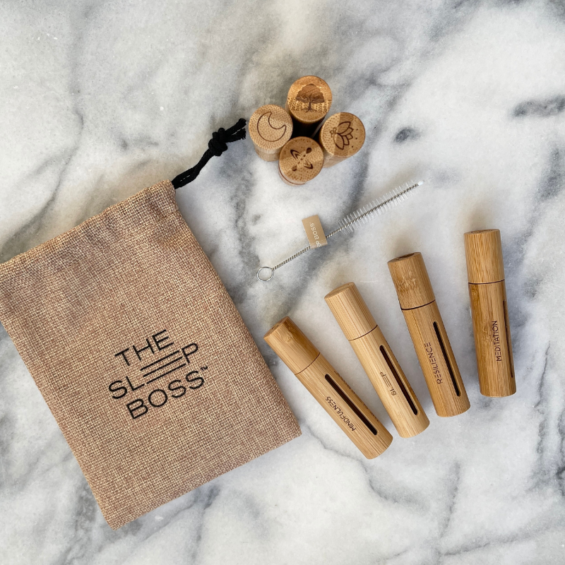 Set of engraved bamboo essential oil rollers with a carrying pouch labelled 'The Sleep Boss' on a marble surface.